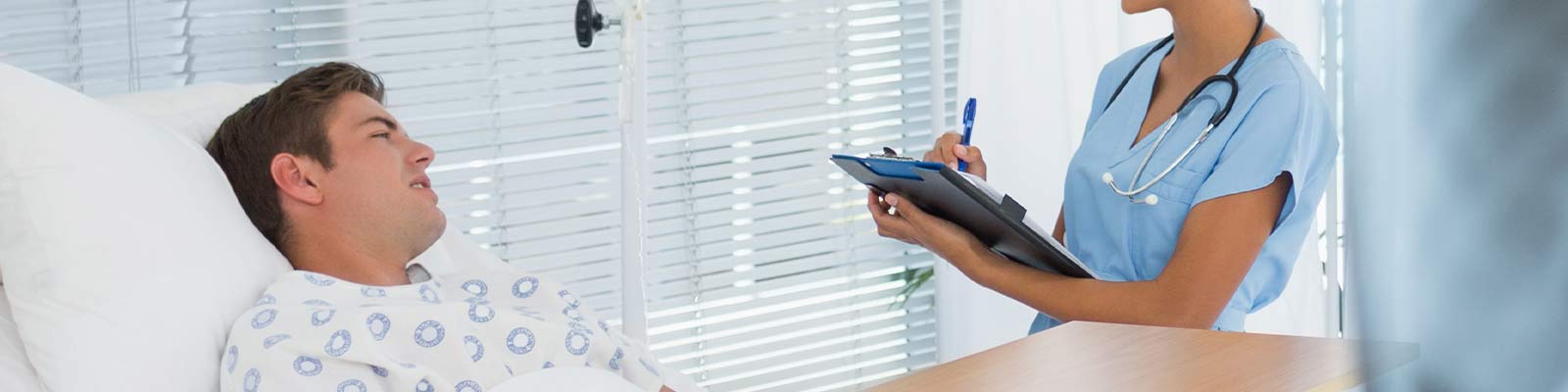 nurse with a pen and chart talking to a patient in a hospital bed